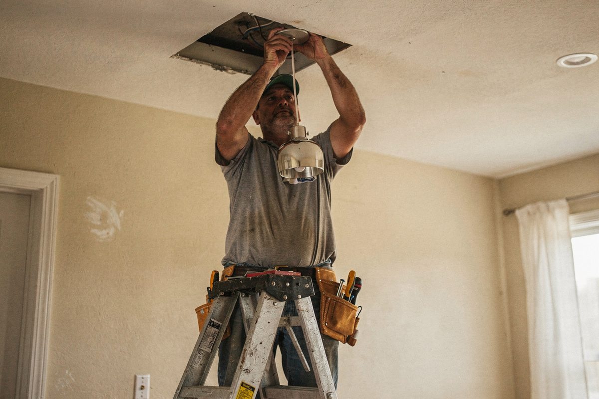 Electrician installing a pendant light fixture from a ladder